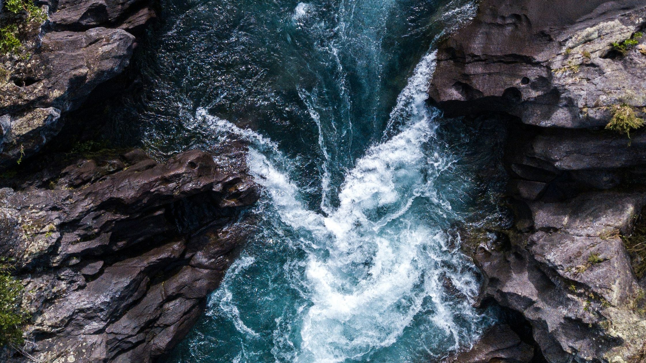 Aerial view of a powerful turquoise river churning through dark, jagged rock canyon walls