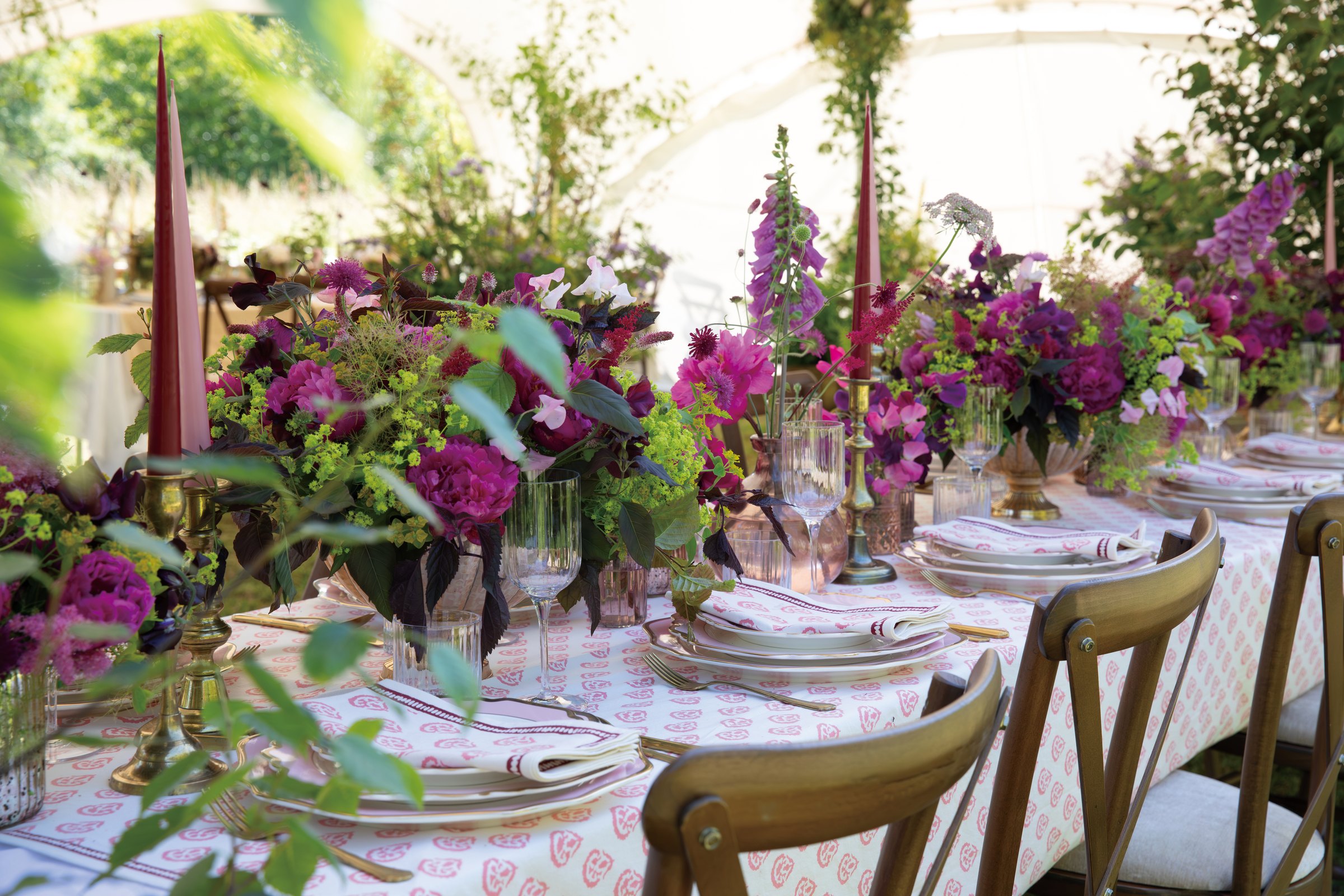 A long table under a marquee, laid with flowers and candles