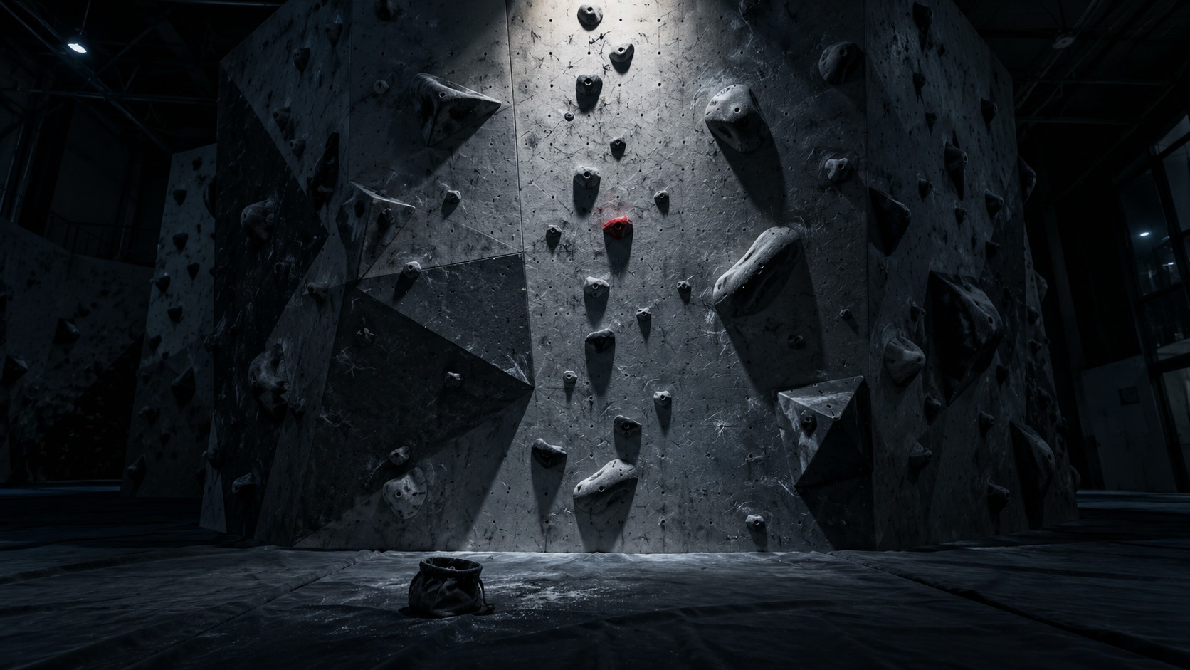 Parete di arrampicata di notte: appigli grigi in fila su un pannello, un solo appiglio rosso a metà via, un sacchetto di magnesite aperto sul materasso.