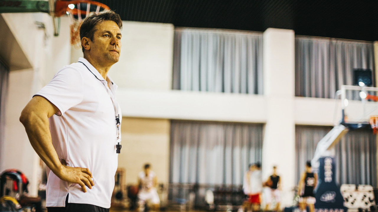 Basketball coach standing courtside with hands on hips