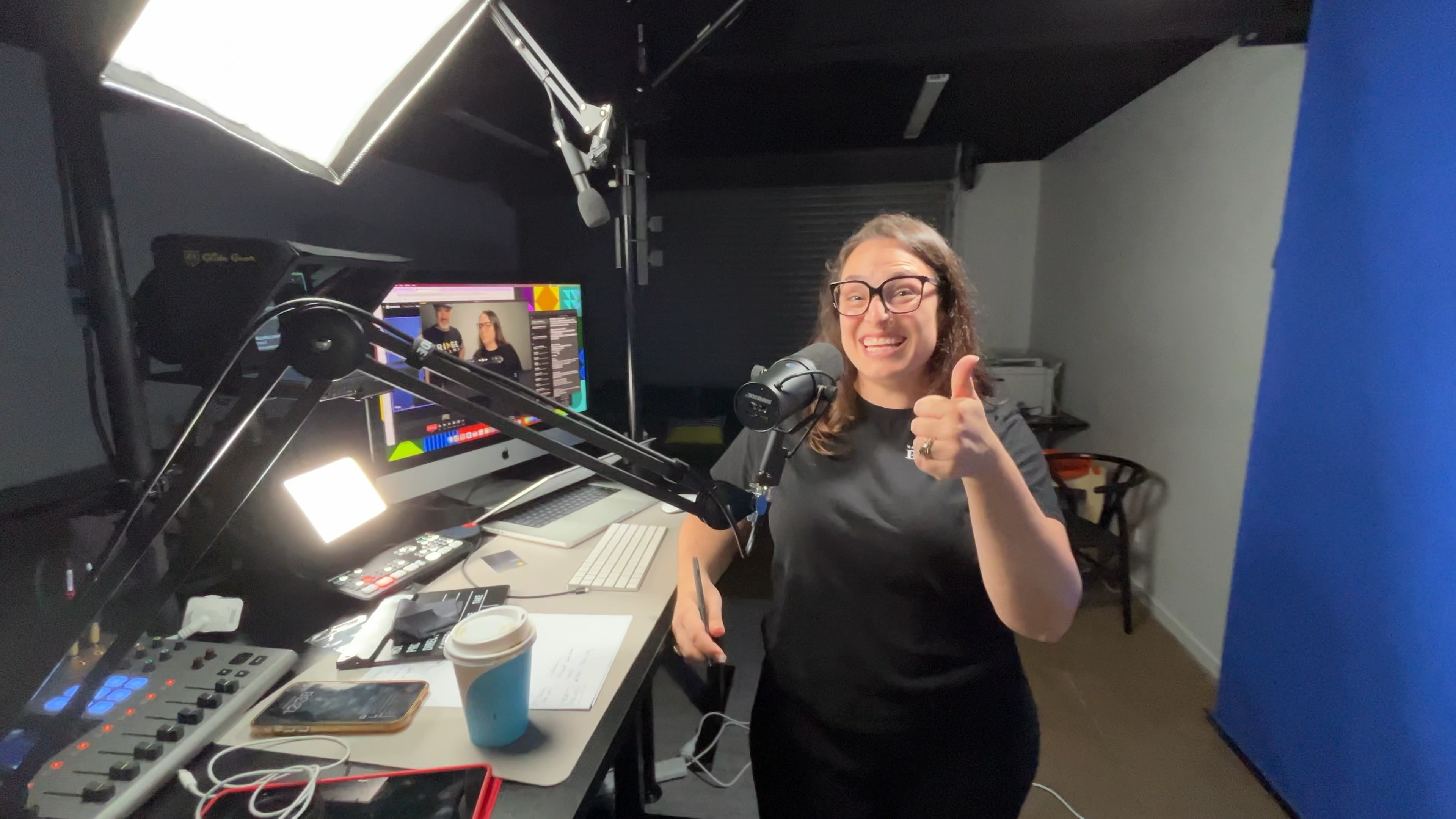 A smiling Ridge client giving a thumbs up in her studio beside a podcast mic, softbox and blue backdrop