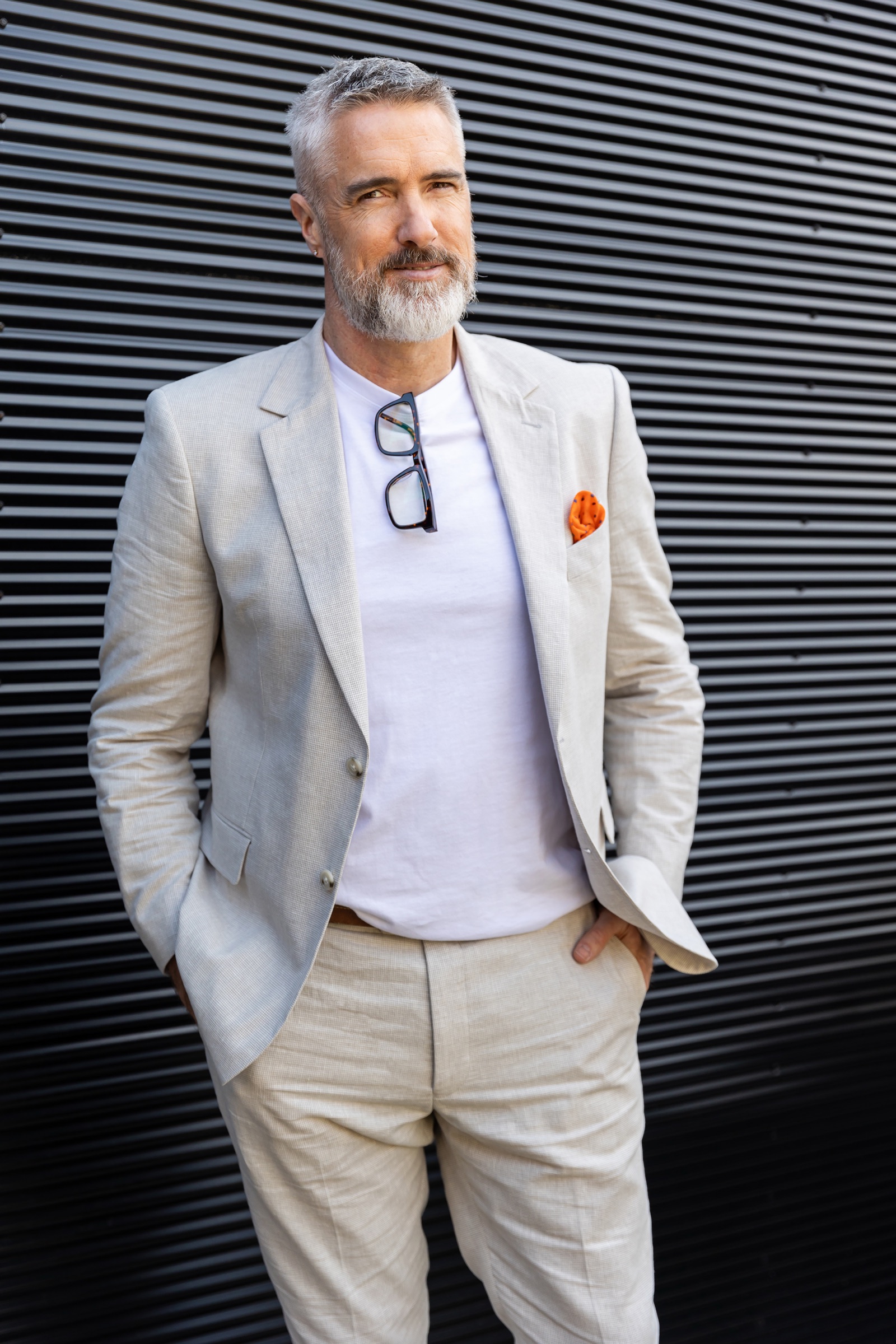 Chris Schwager standing on a street in a beige suit, hands in pockets, looking at the camera