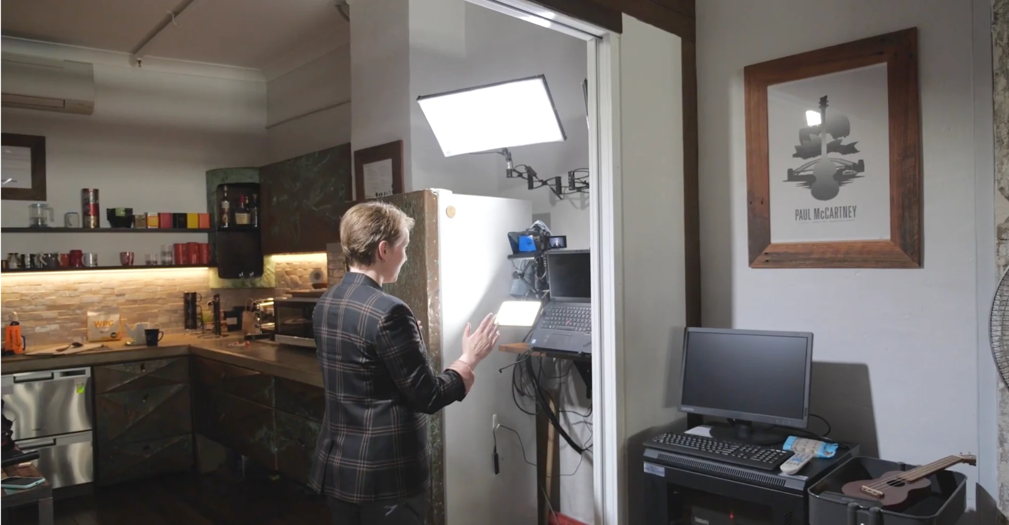 Heather Hukins before: adjusting a light and camera set up in a doorway beside the office kitchen