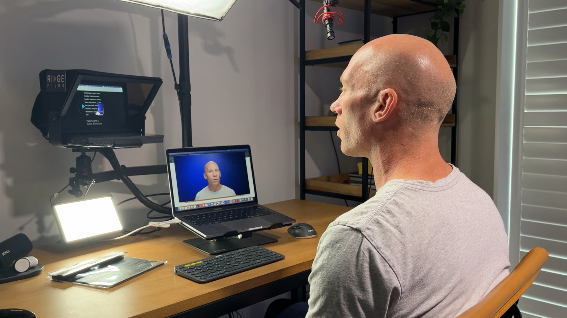 A Ridge client in profile recording at his desk, his script on the teleprompter in front of the lens