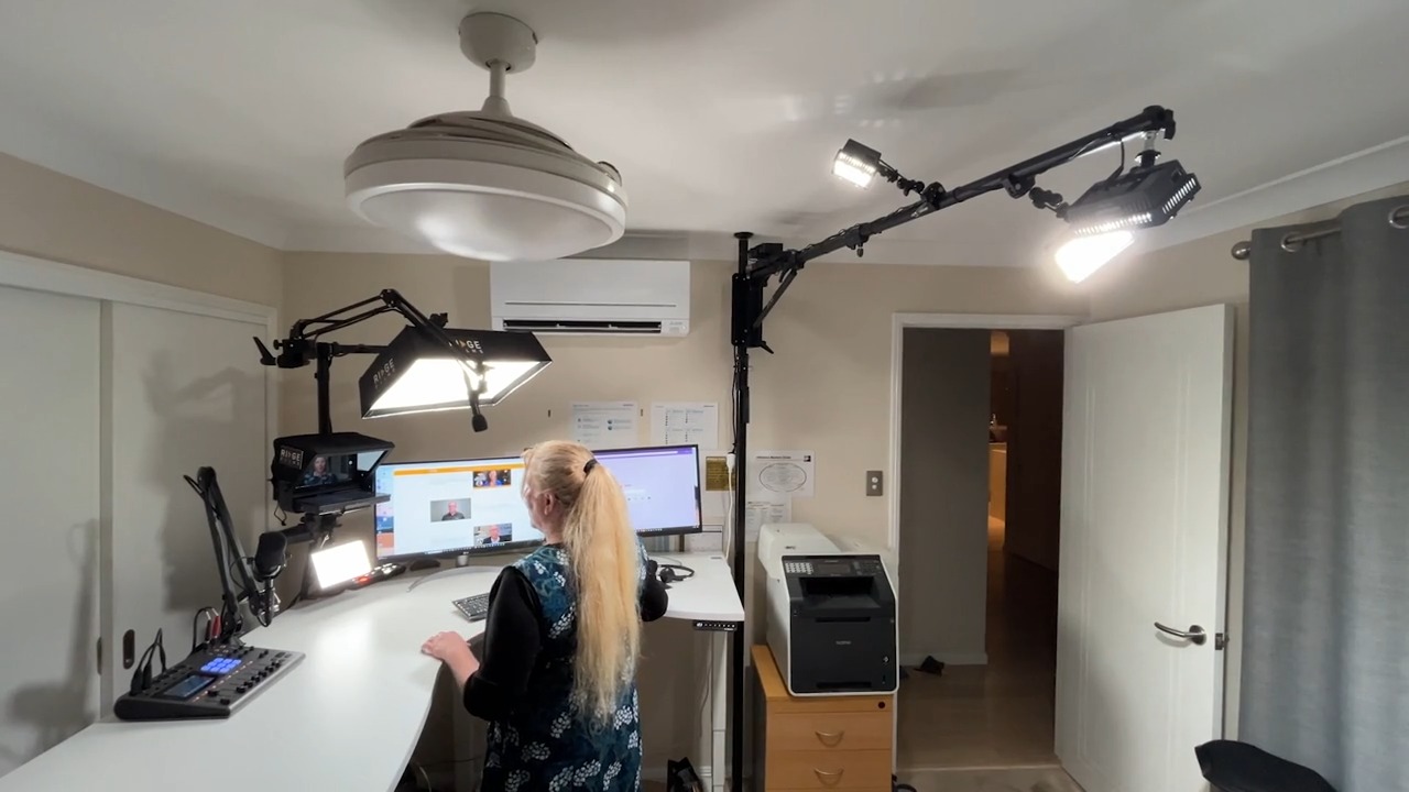 A Ridge client at her curved standing-desk studio with two monitors, teleprompter and track spotlights