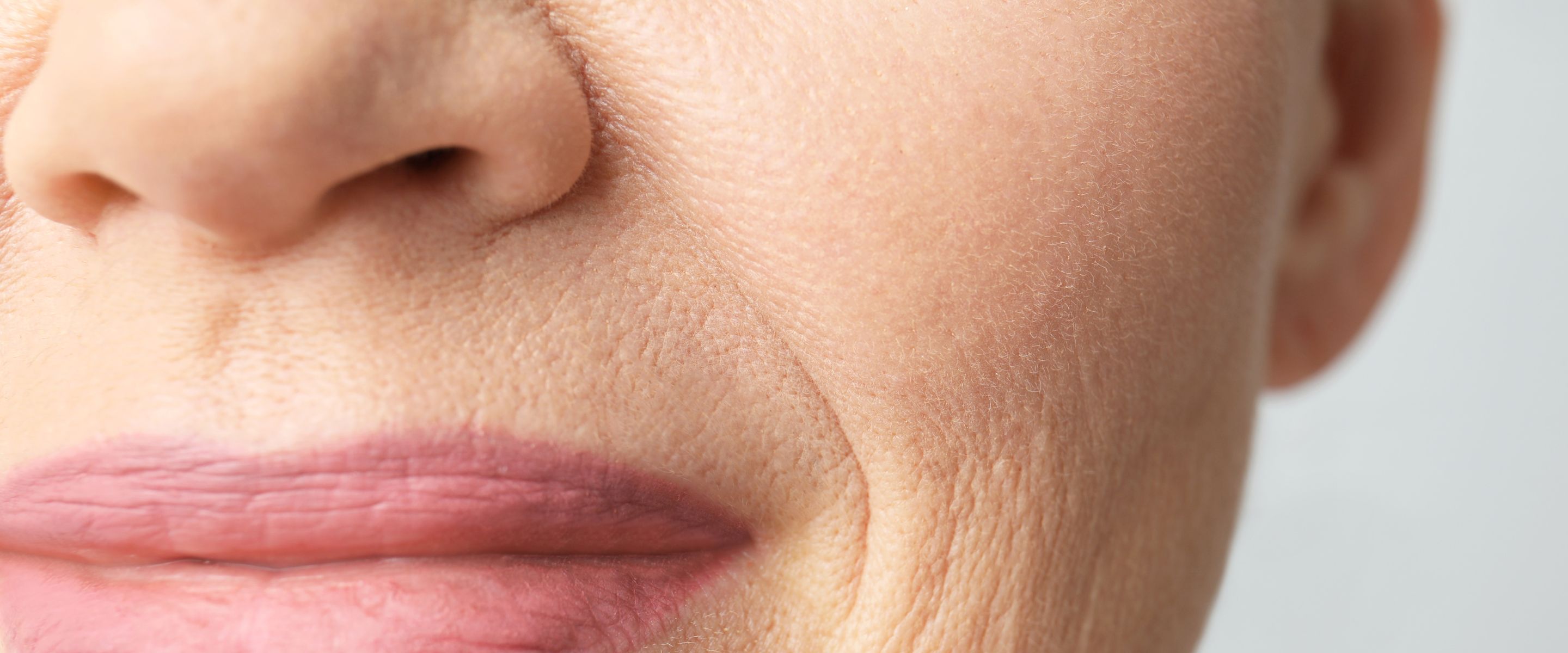 Close-up of an older woman's lower face in soft light, lines and natural skin texture visible.