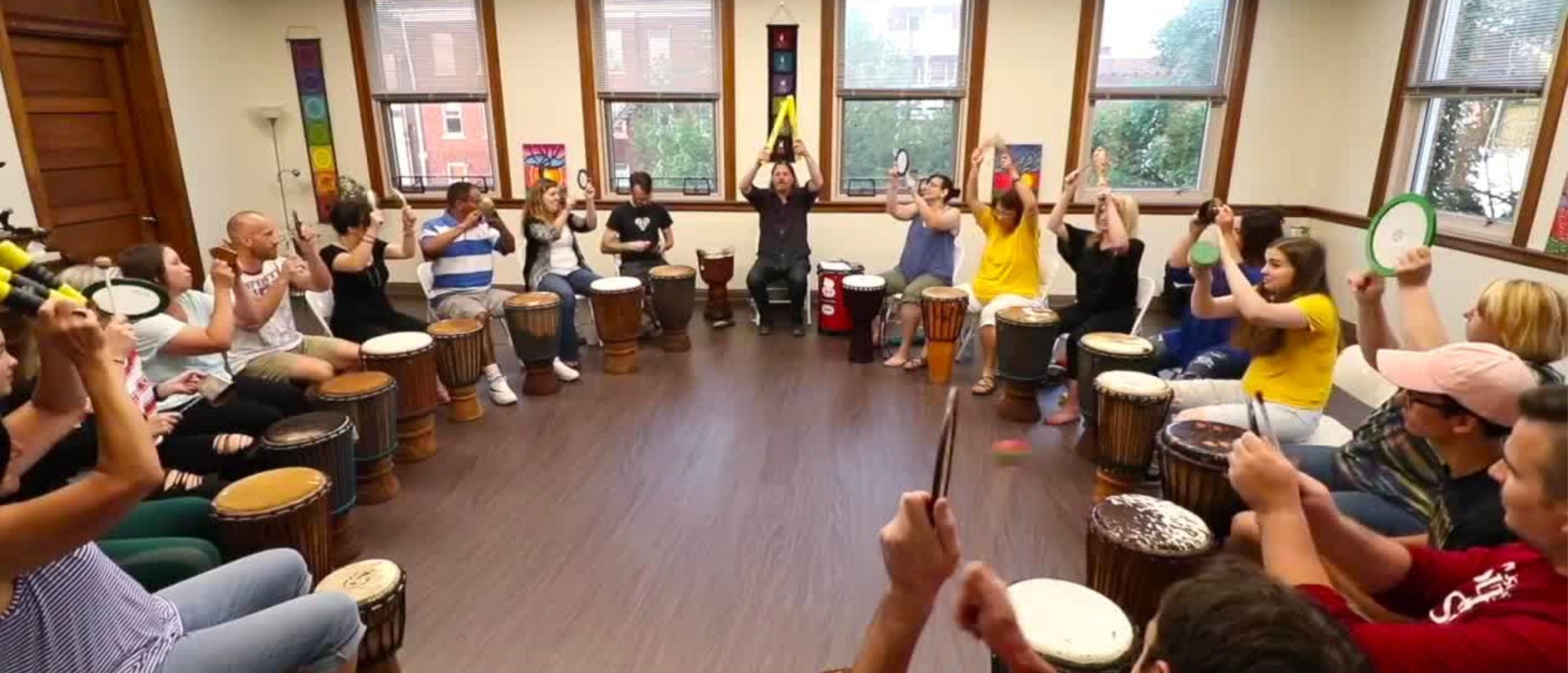 A full drum circle of adults seated together with hand drums during a live training