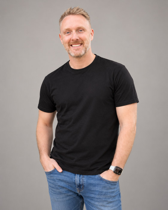 Anthony Price smiling in a black T-shirt and jeans with his hands in his pockets