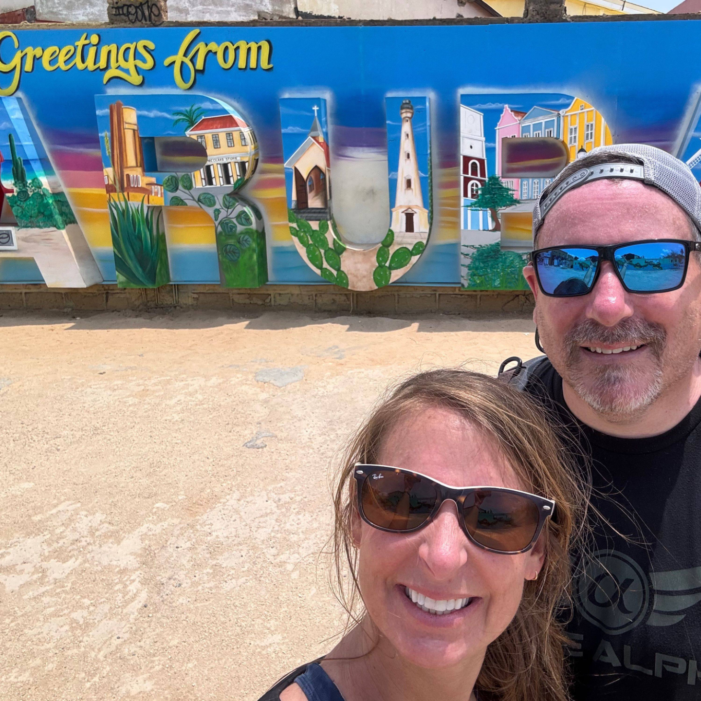 scott and melissa in front of colorful painted aruba sign