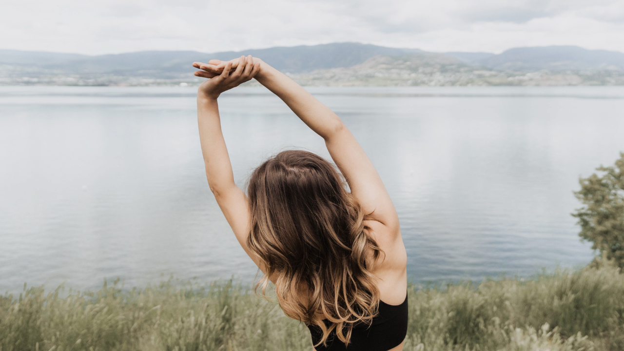 Woman stretching arms overhead by a mountain lake — on taking your restoration seriously as a female founder