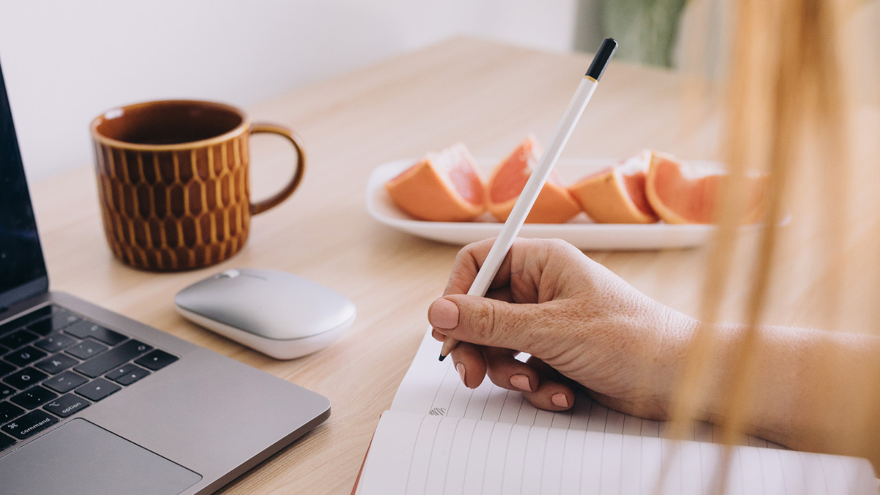 Woman journaling at a desk with laptop and coffee, symbolising creativity, content creation, and authentic voice