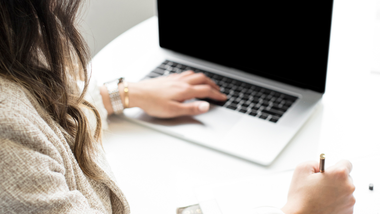 Woman working on laptop at desk, writing notes