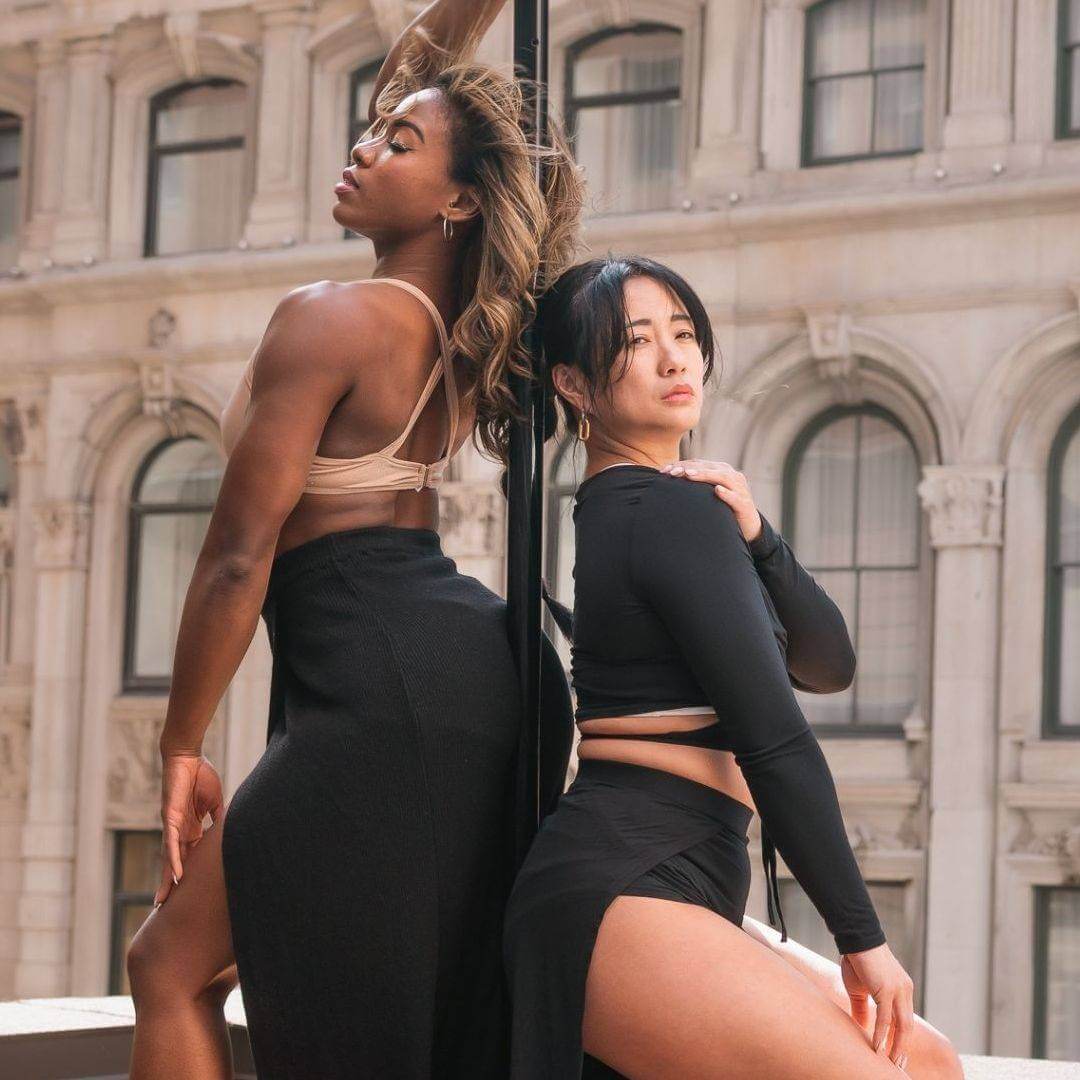 Two dancers posing beside a pole at Milan Pole Dance Studio, where students learn to pole dance