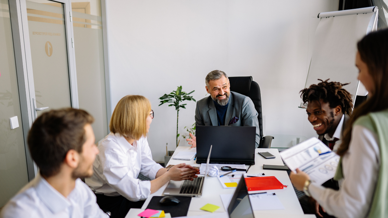 Image of teachers sitting at a table meeting.  They have papers and computers in front of them.
