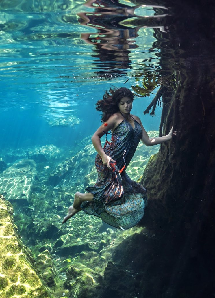 Woman in a flowing dress underwater in a cenote