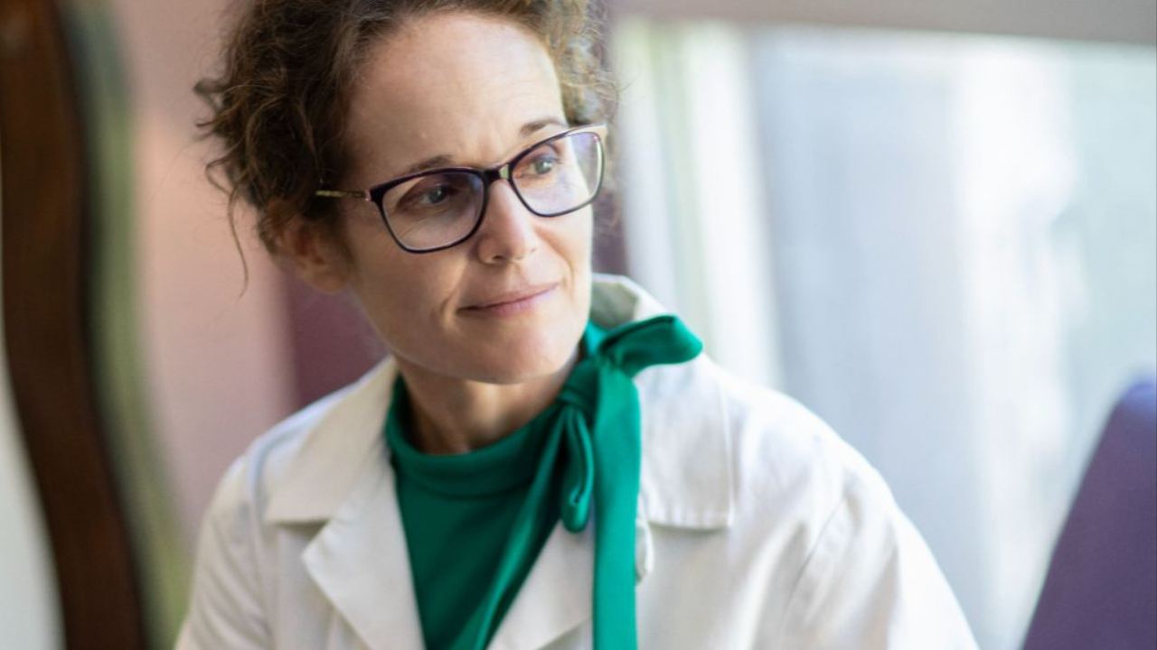 Dr Wendy in white coat and kelly green dress looking off to the right side pensively as she contemplates designing better ways to practice, relate and prevent eating disorders