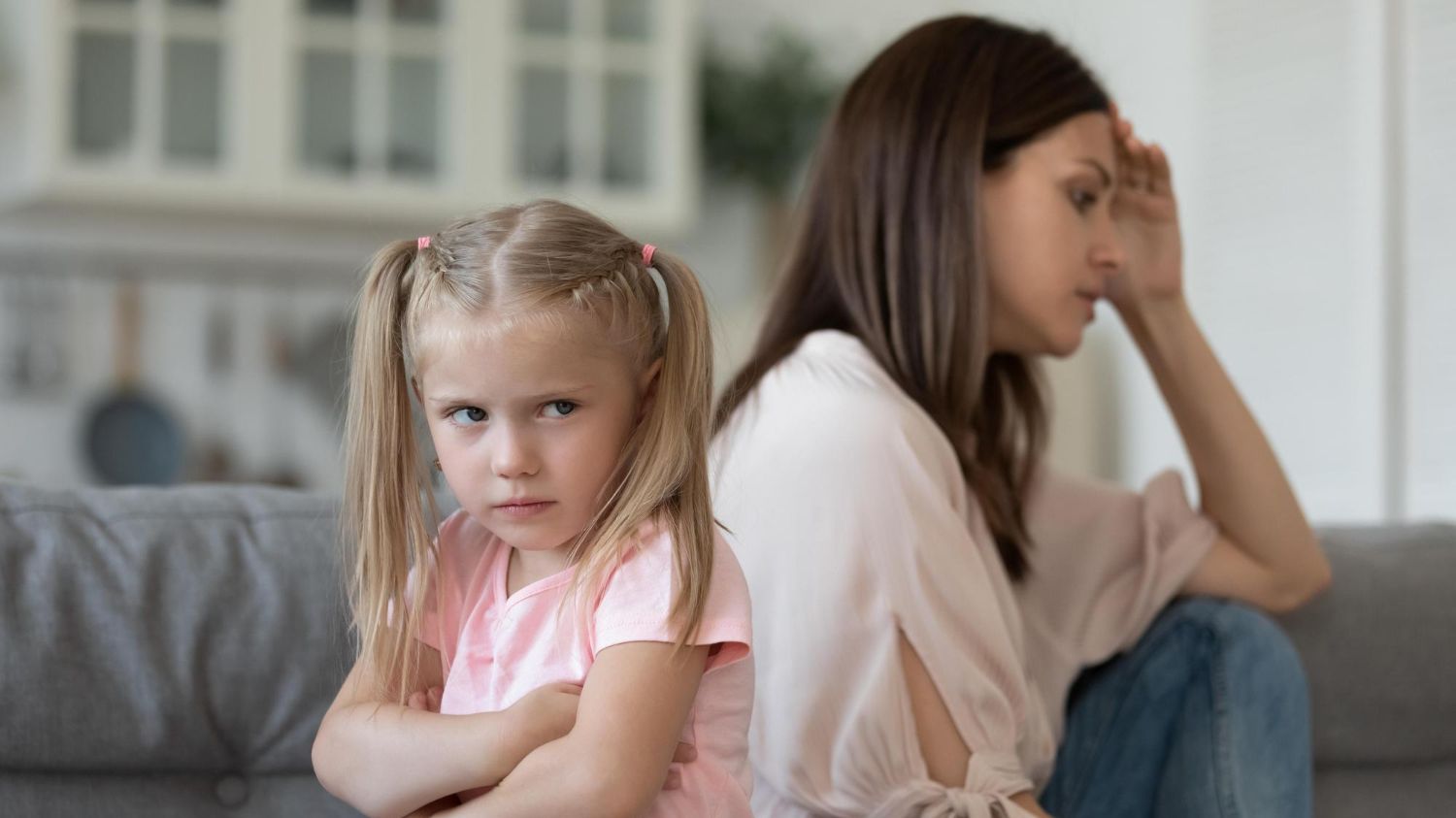 Parent and strong-willed child sitting apart after a conflict, showing frustration and disconnection