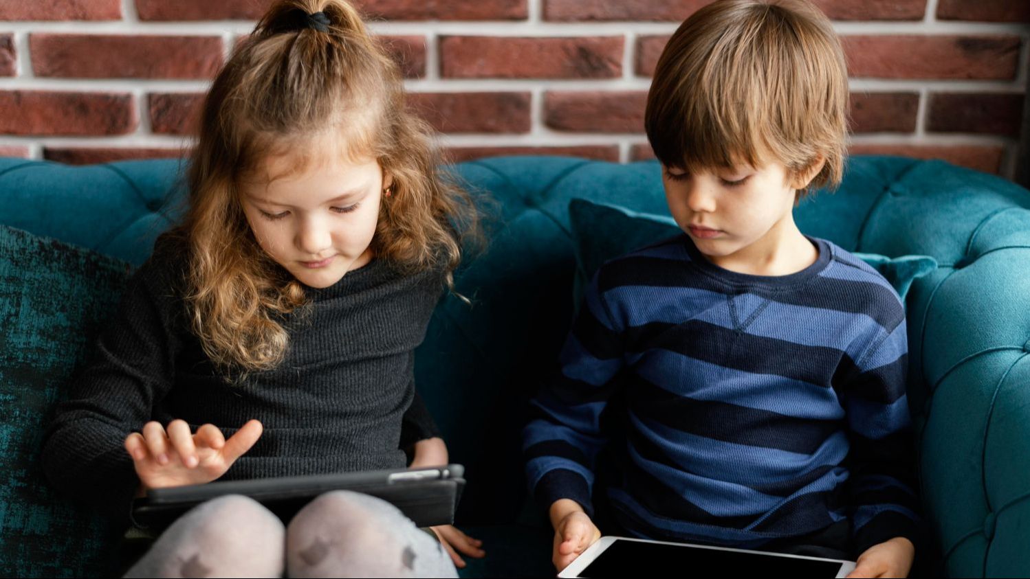 Young children using tablets on a couch at home