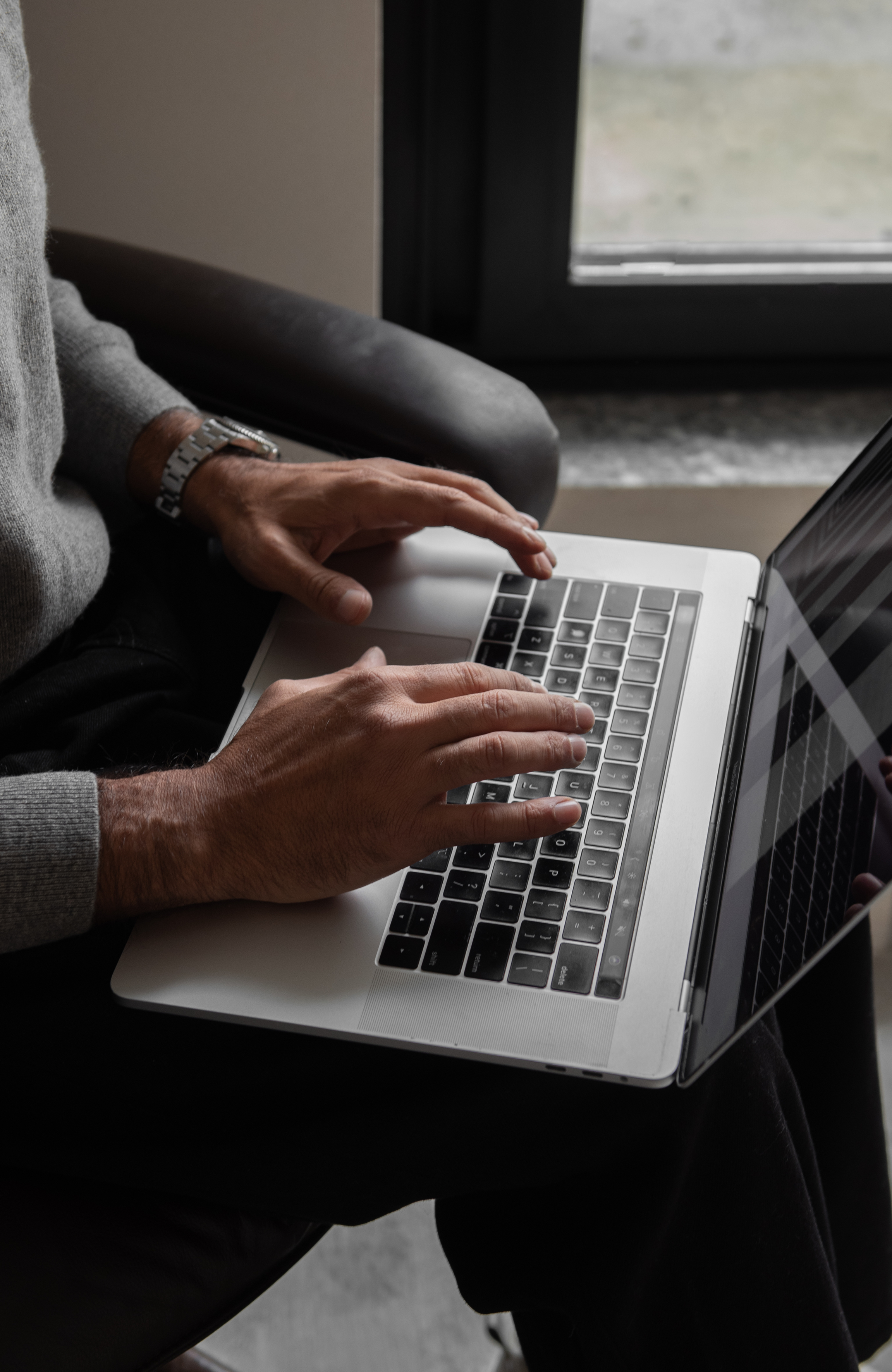 Hands typing on a laptop by a window