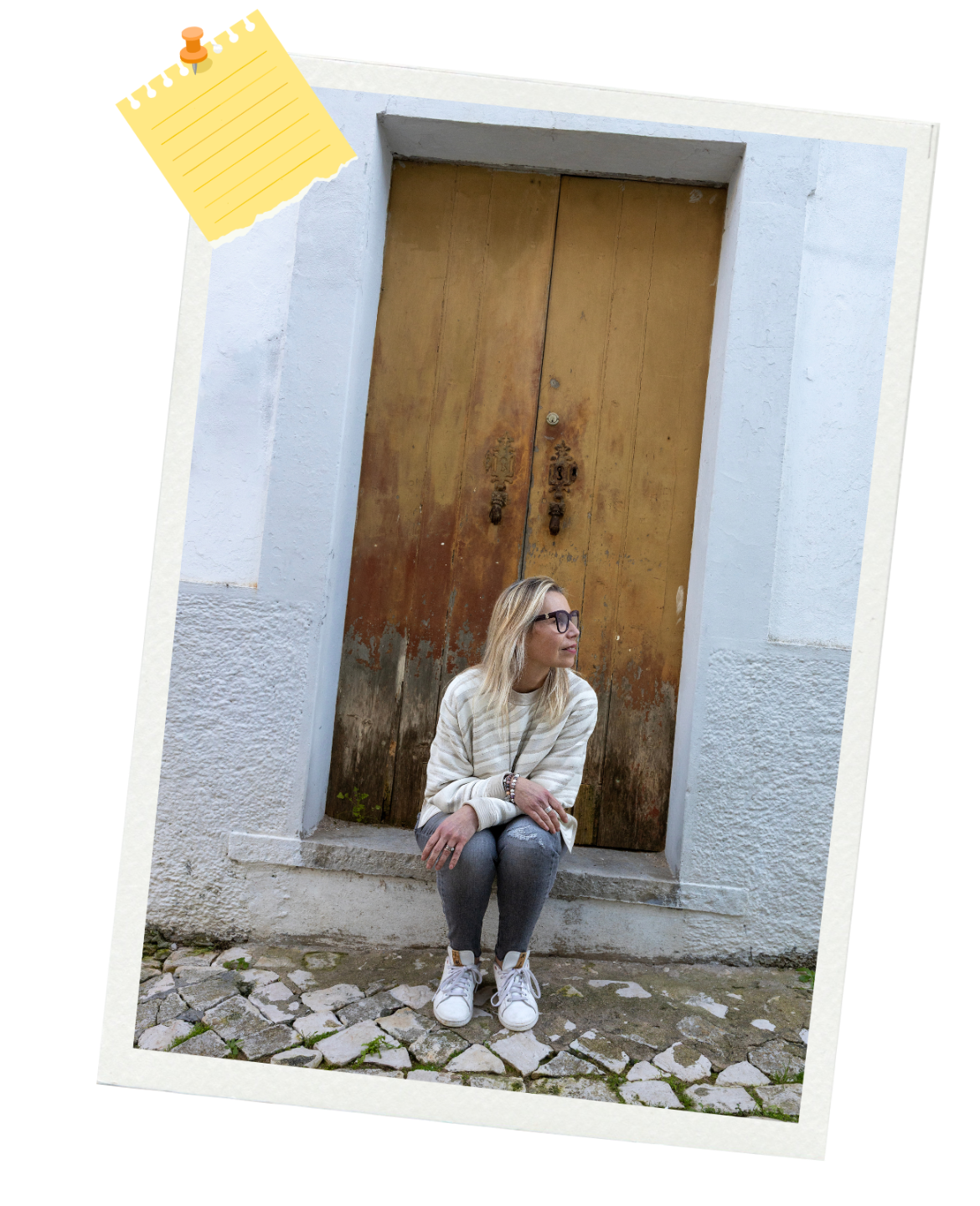 Andrea with blonde hair and glasses sits on a stone step in front of a large, worn wooden door, looking to her right. The image has a taped note graphic in the corner.