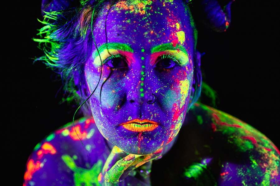 A trick photograph of a woman's face glowing with colourful glow in the dark neon paint under UV black light. Learn how to do black light photography with this tutorial.