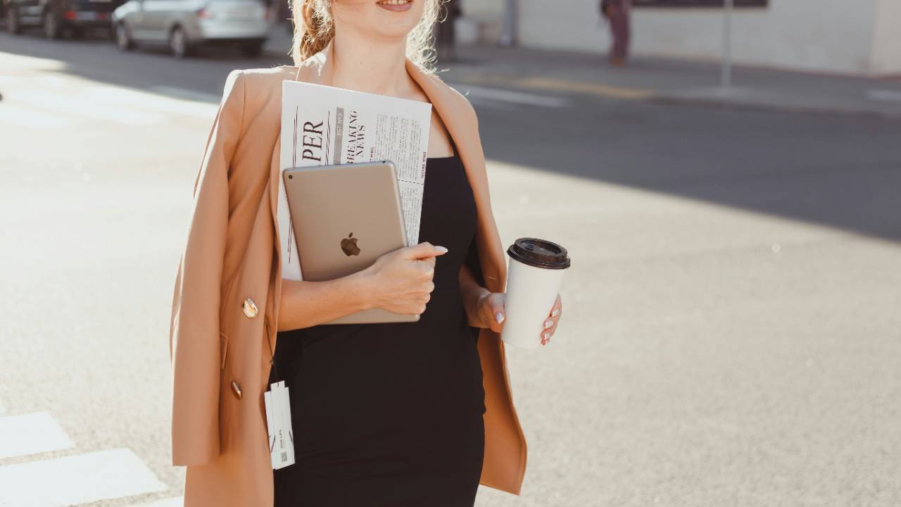 Woman in black dress with camel blazer, coffee, iPad, and newspaper