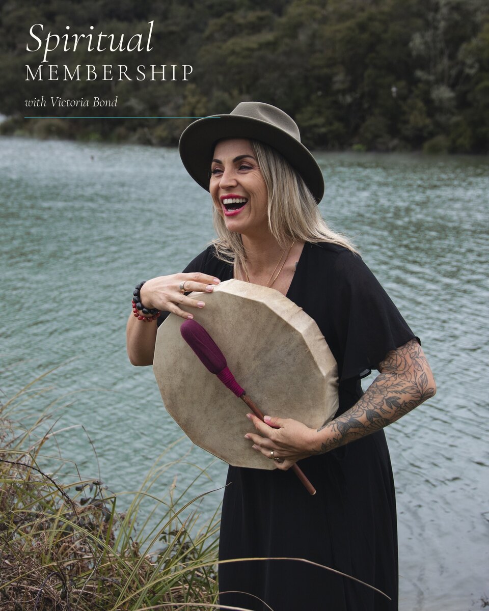 Victoria laughing as she holds a hand drum by a lake.