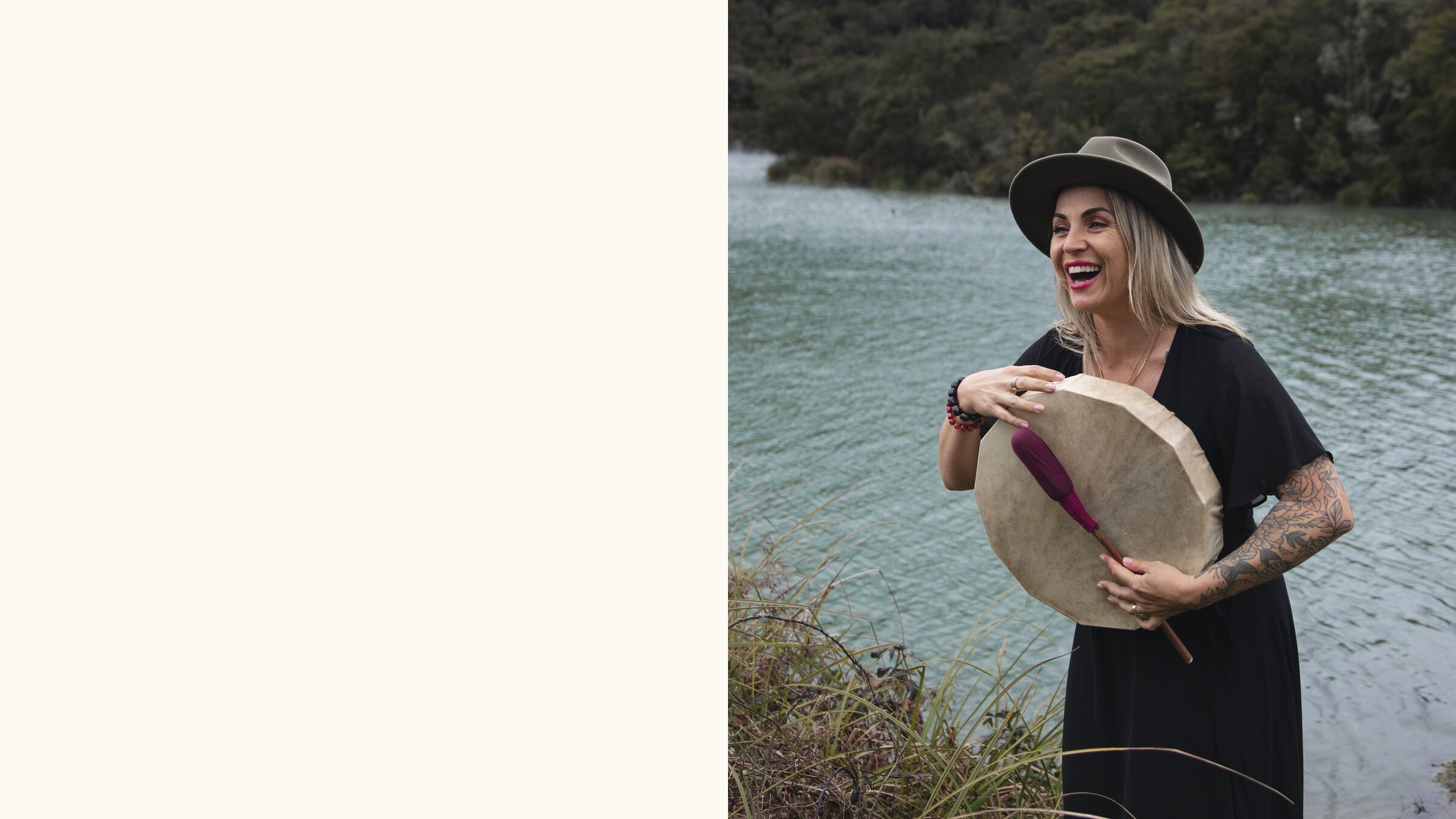 Victoria Bond laughing in an olive hat by the lake, holding a frame drum