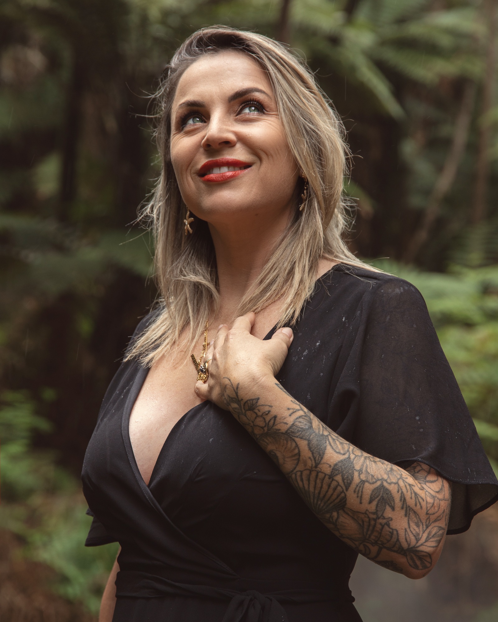 Victoria Bond standing among native New Zealand ferns, one hand at her heart, looking up.