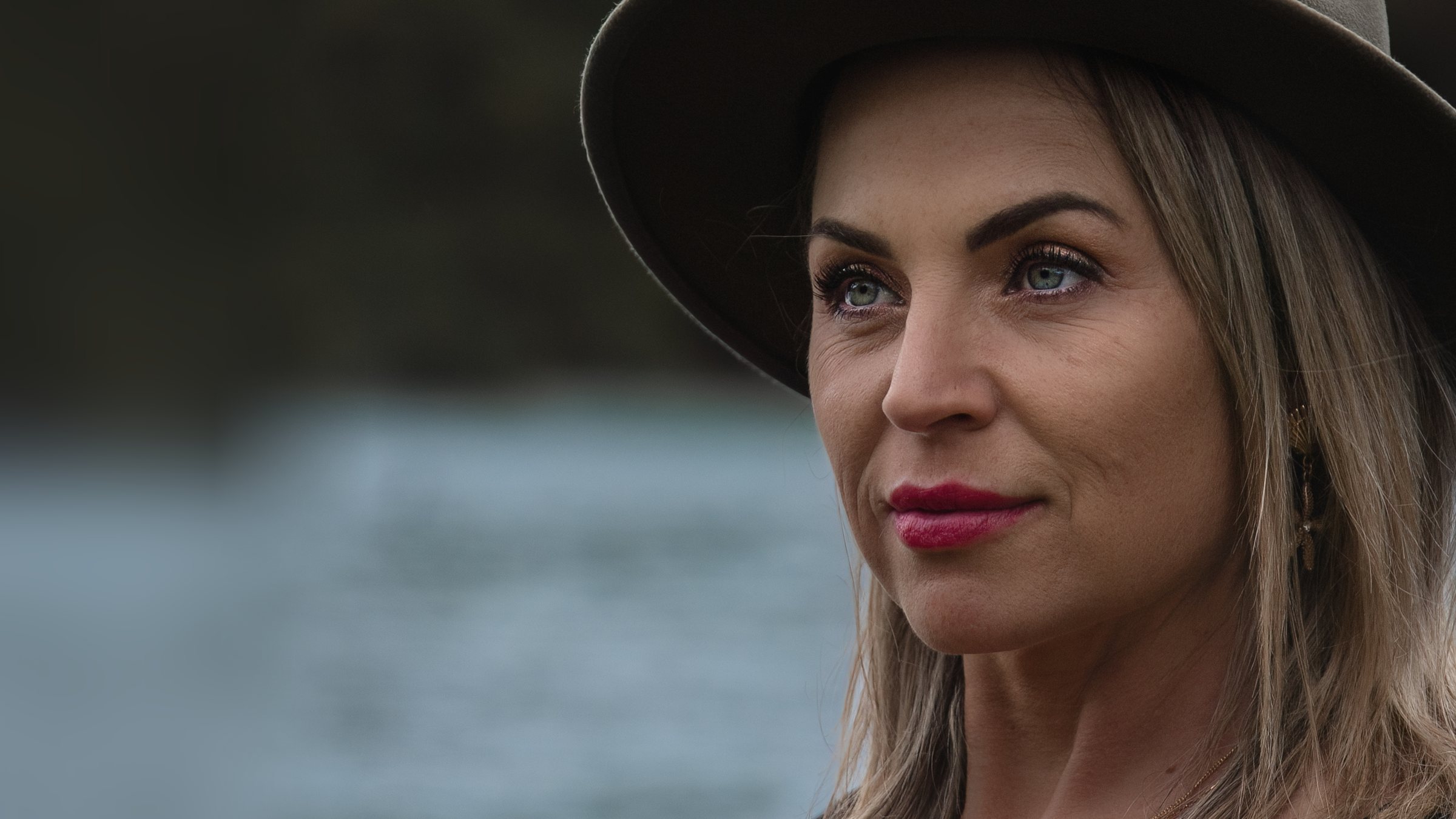 Victoria Bond in close profile under the brim of her hat, a soft lake behind her