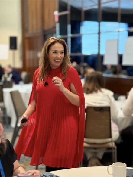 Jennifer Krueger in a red dress laughing with a room of salespeople
