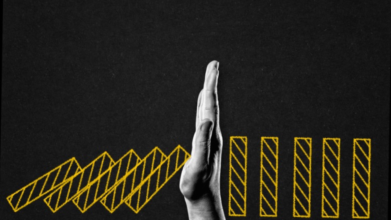 hand stopping dominoes from falling. black background. Yellow dominoes.