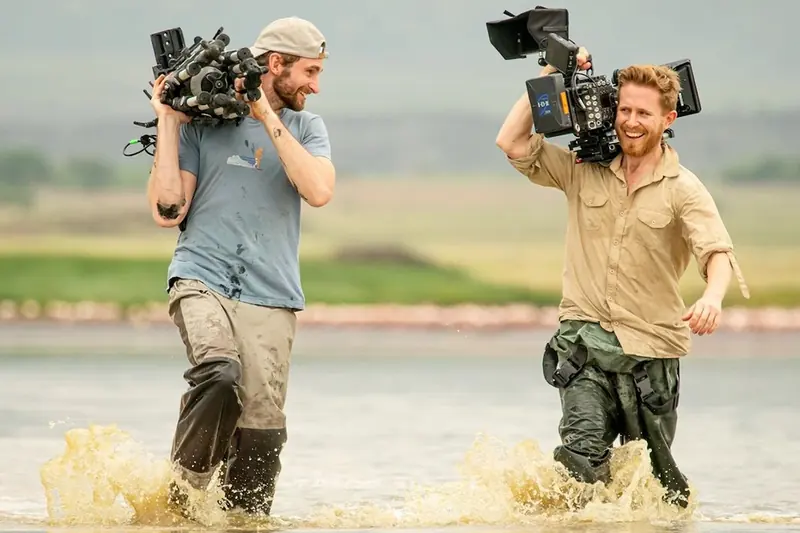 Sebastian and Duncan wading through a lake with cameras on their shoulders