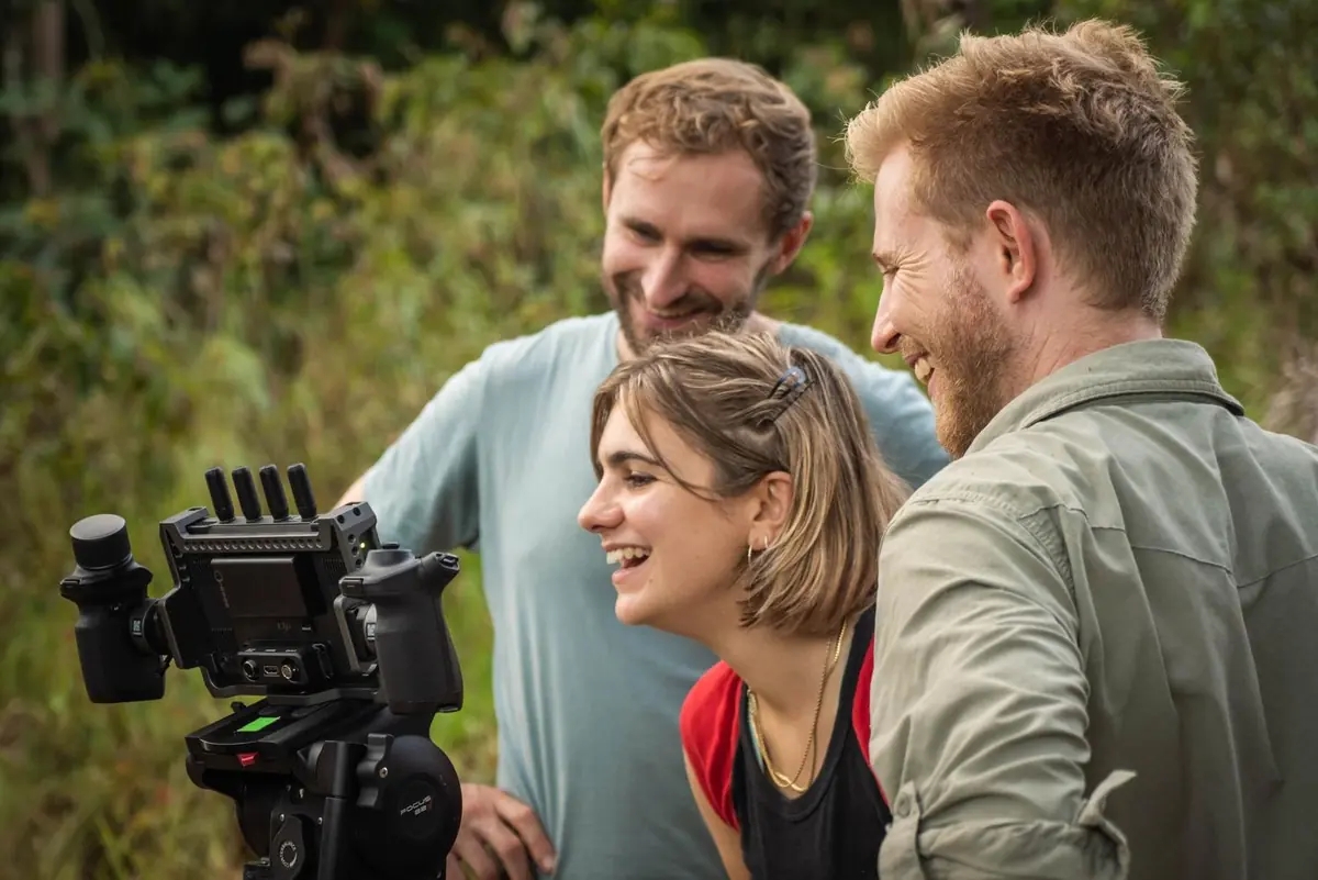 Three people laughing together as they watch footage back on a camera monitor in the field