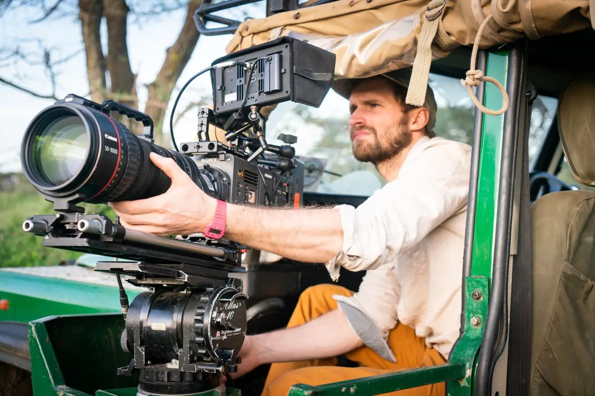A cameraman filming with a long lens mounted on the door of a Land Rover