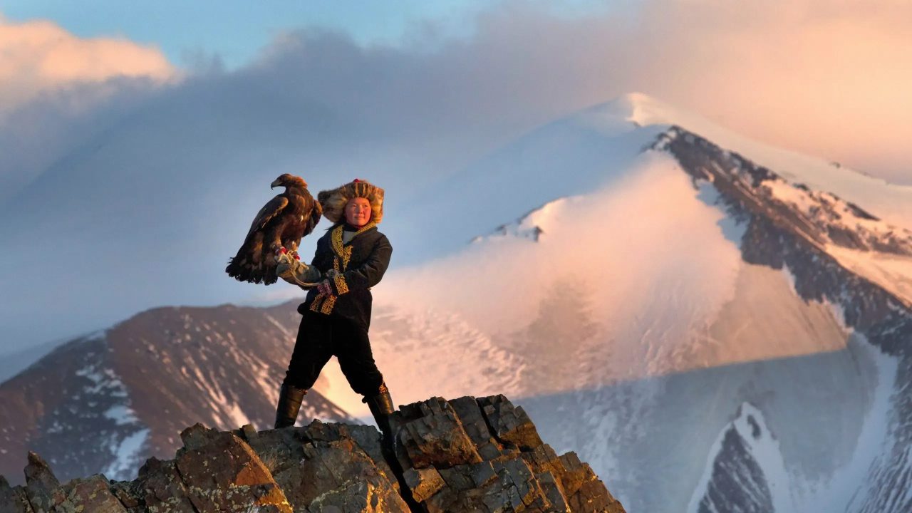 Eagle Huntress documentary trailer example - filmmaker standing on mountain with eagle