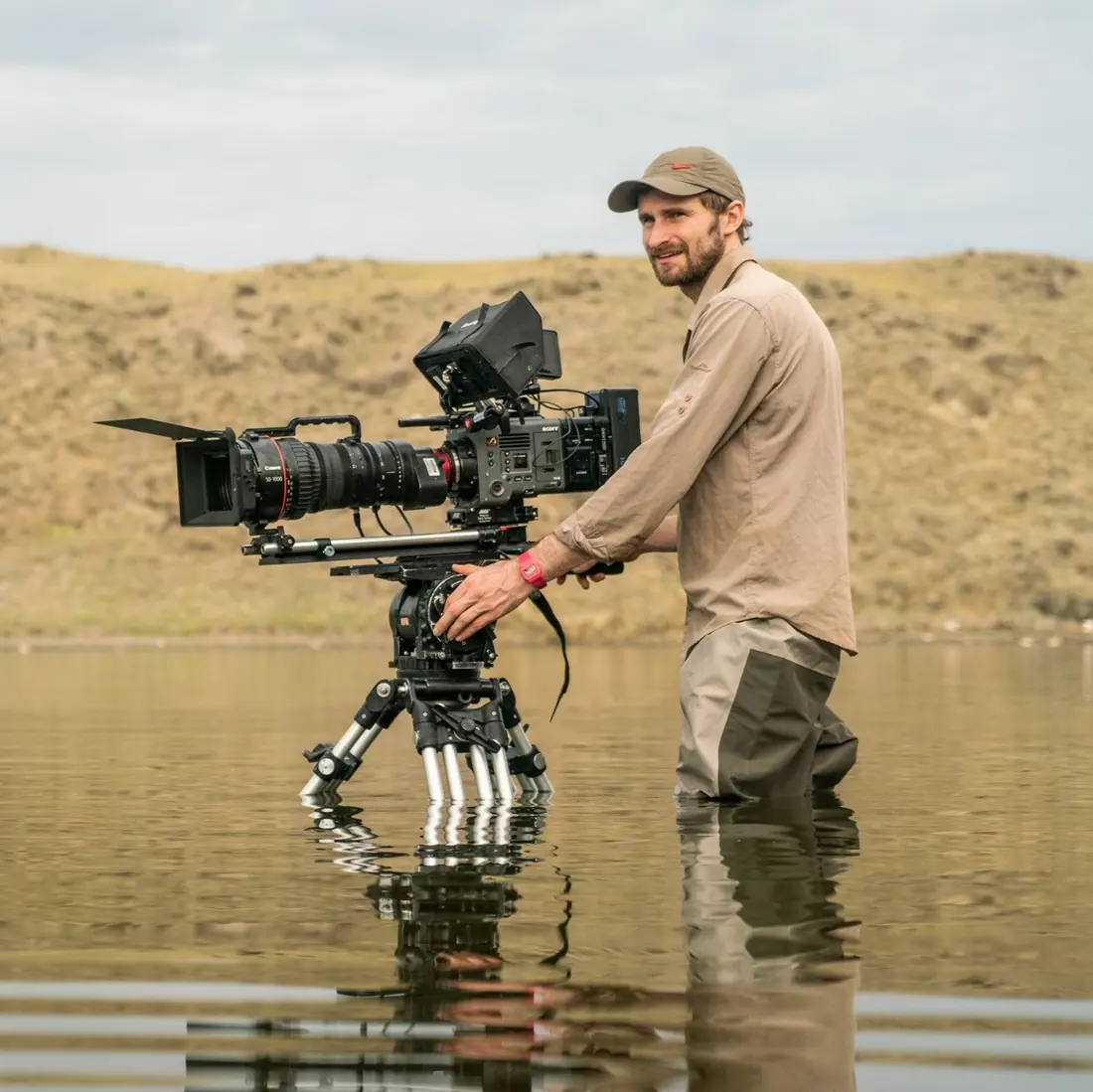 Duncan in waders, standing in a lake beside a long-lens camera on a tripod and smiling