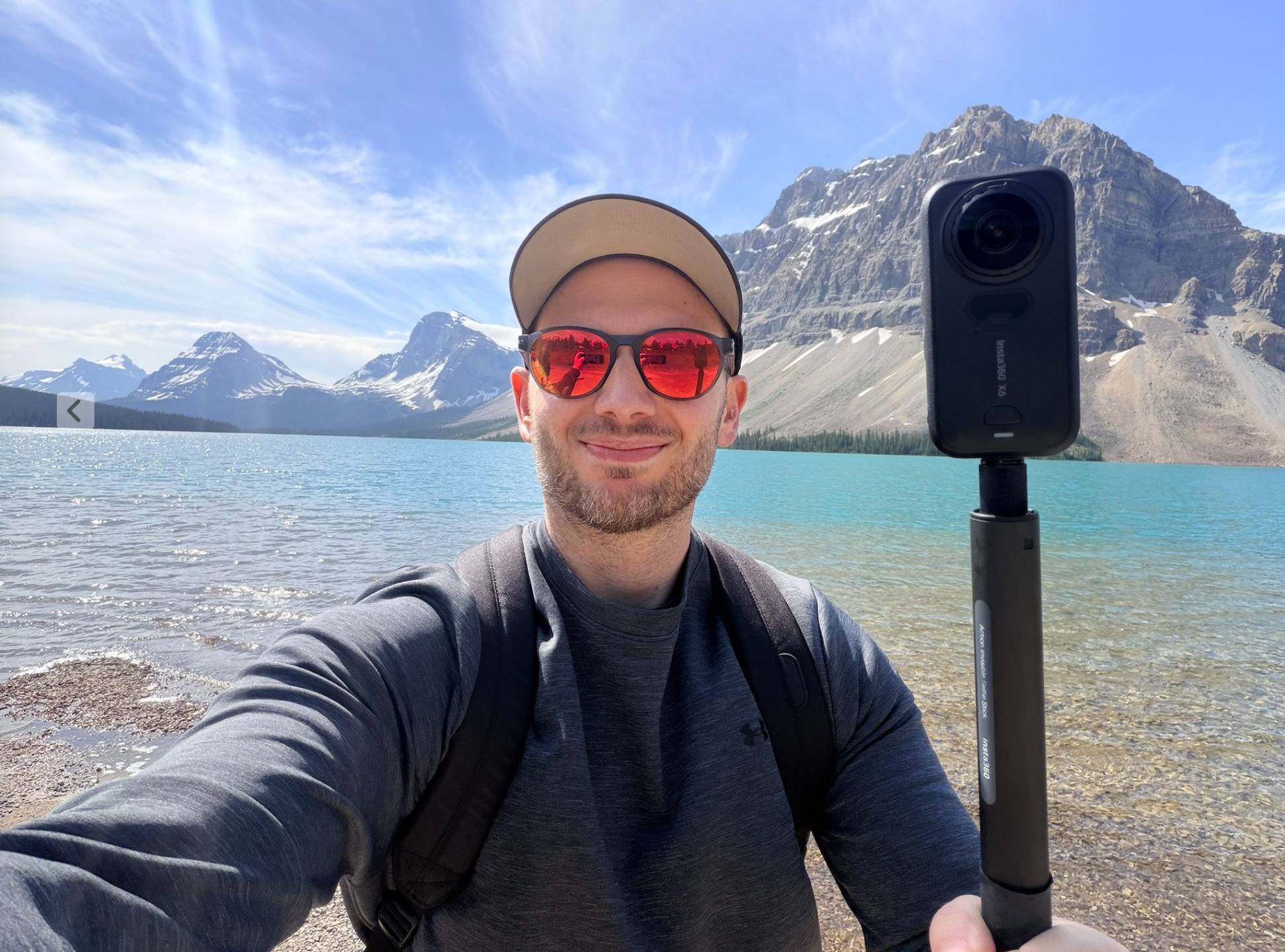 Ben beside a mountain lake holding his Insta360 X6 on an Action Invisible Selfie Stick.