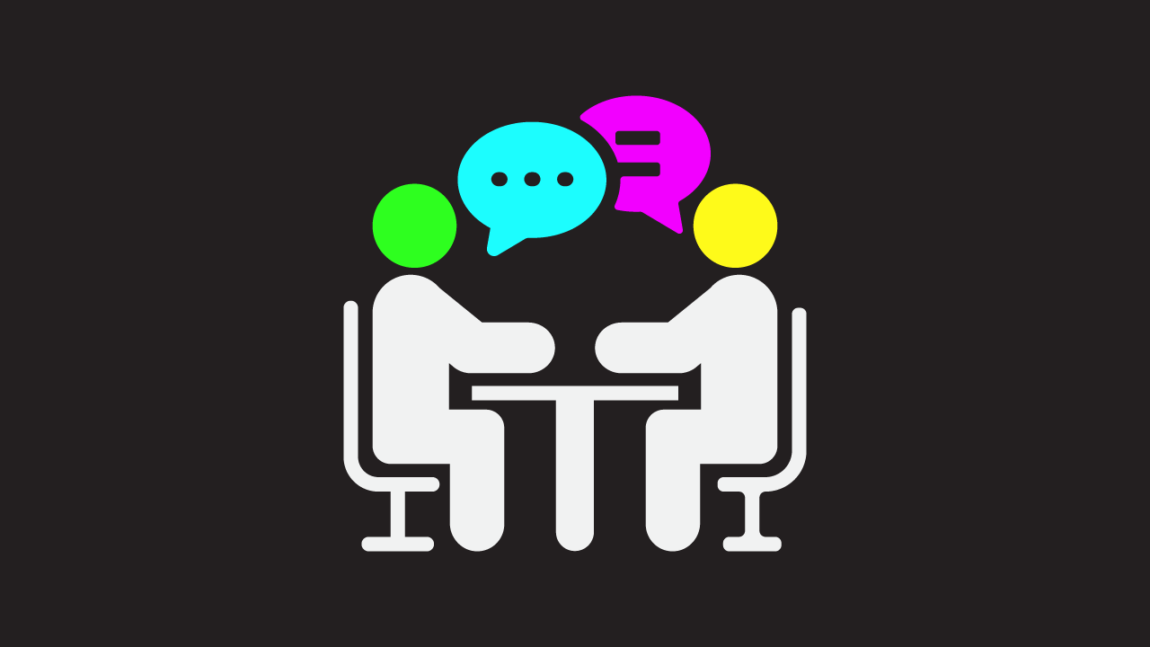 Two icons representing people are sat on chairs at a table facing each other. One person has a yellow coloured head, the other has a green coloured head. Beside both heads are icons of speech bubbles, one with dots symbolising speech, and the other two lines symbolising speech