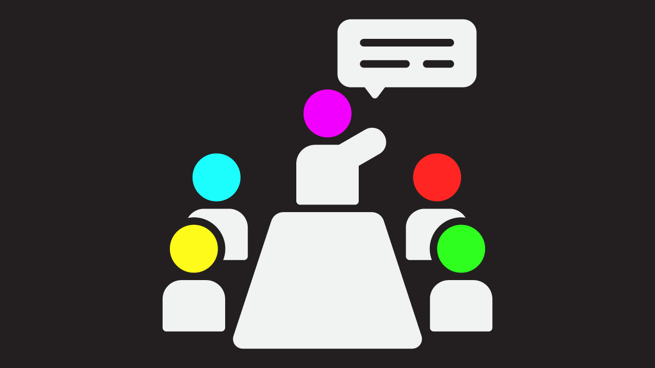 A scene of four icons representing people sat at a table, each with a different coloured head (yellow, teal, red, and green). A person is stood at the front of the table pointing upwards, as if they are teaching. A speech bubble appears from the person standing. This person has a purple coloured head.
