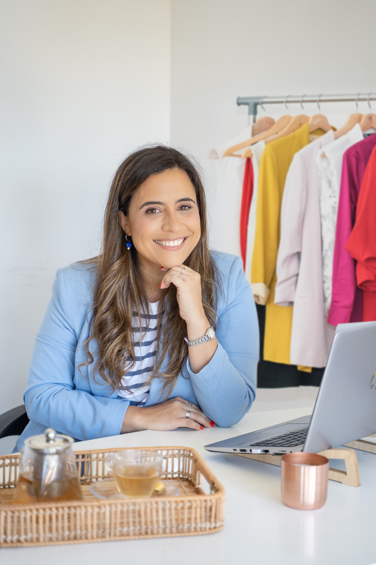 Vicky Zorrilla sonriendo en su escritorio con la notebook, con un perchero de ropa de colores detrás