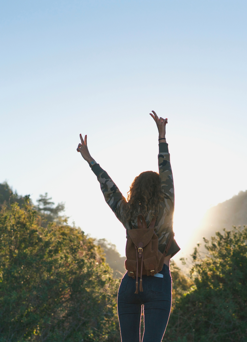 Woman walking outside with arms reaching up with the sun behind her