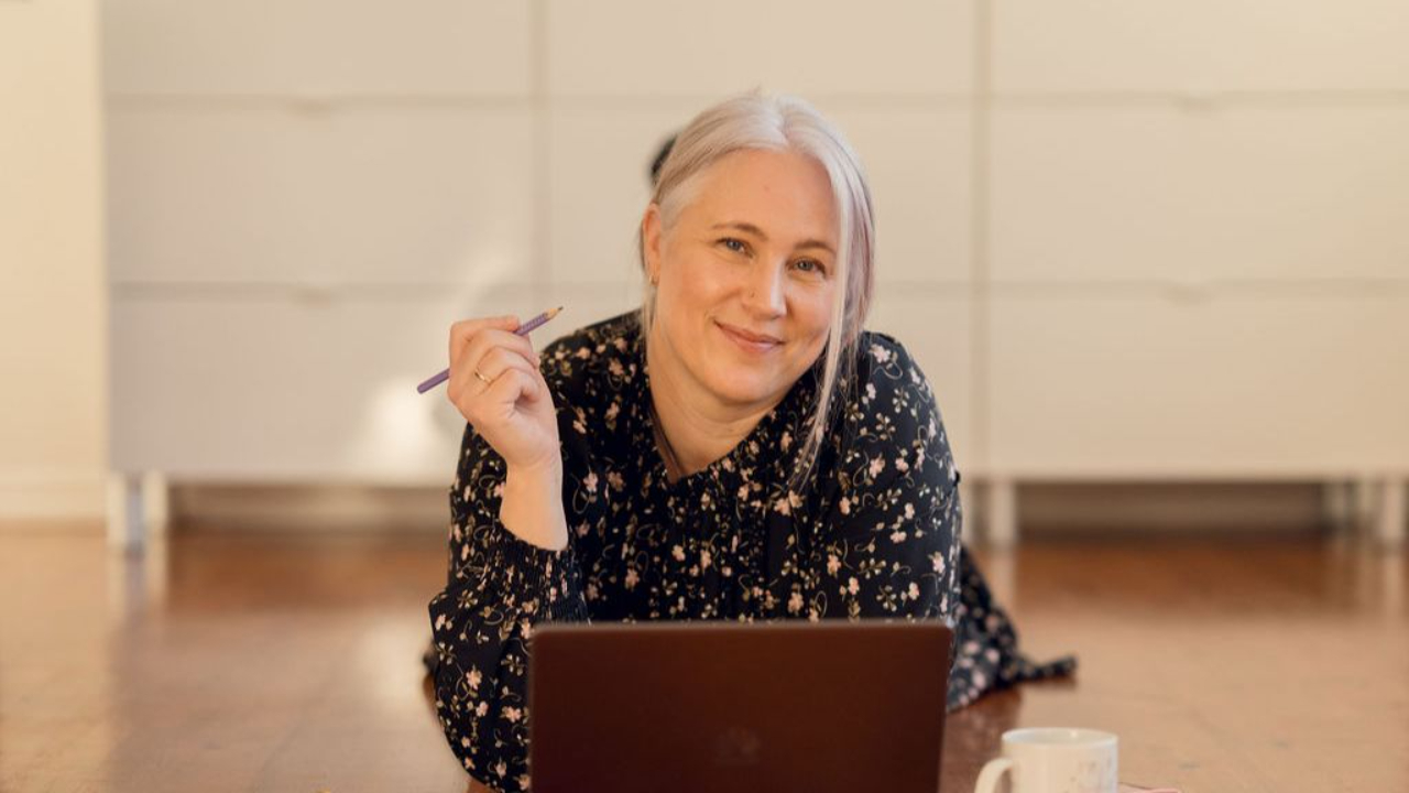 Margrethe ligger på gulvet, kikker i kamera og smiler.