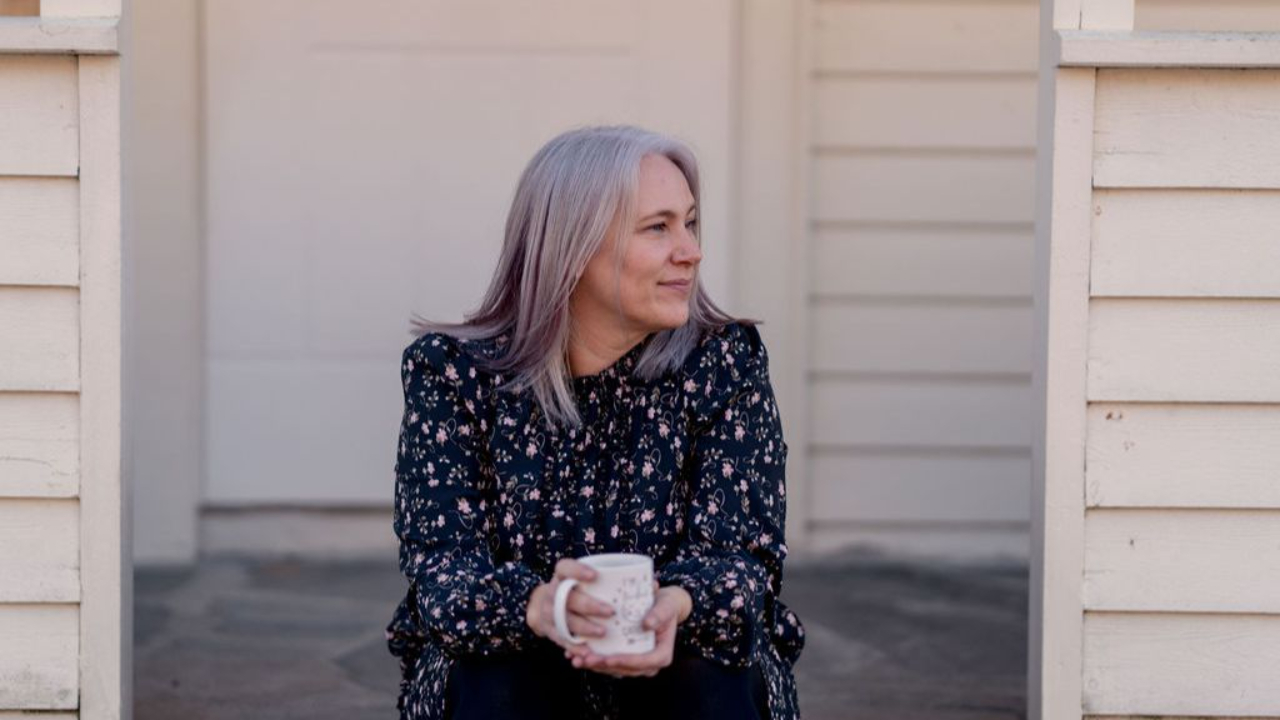 Margrethe sitter på trappa med kaffekopp og kikker til siden.