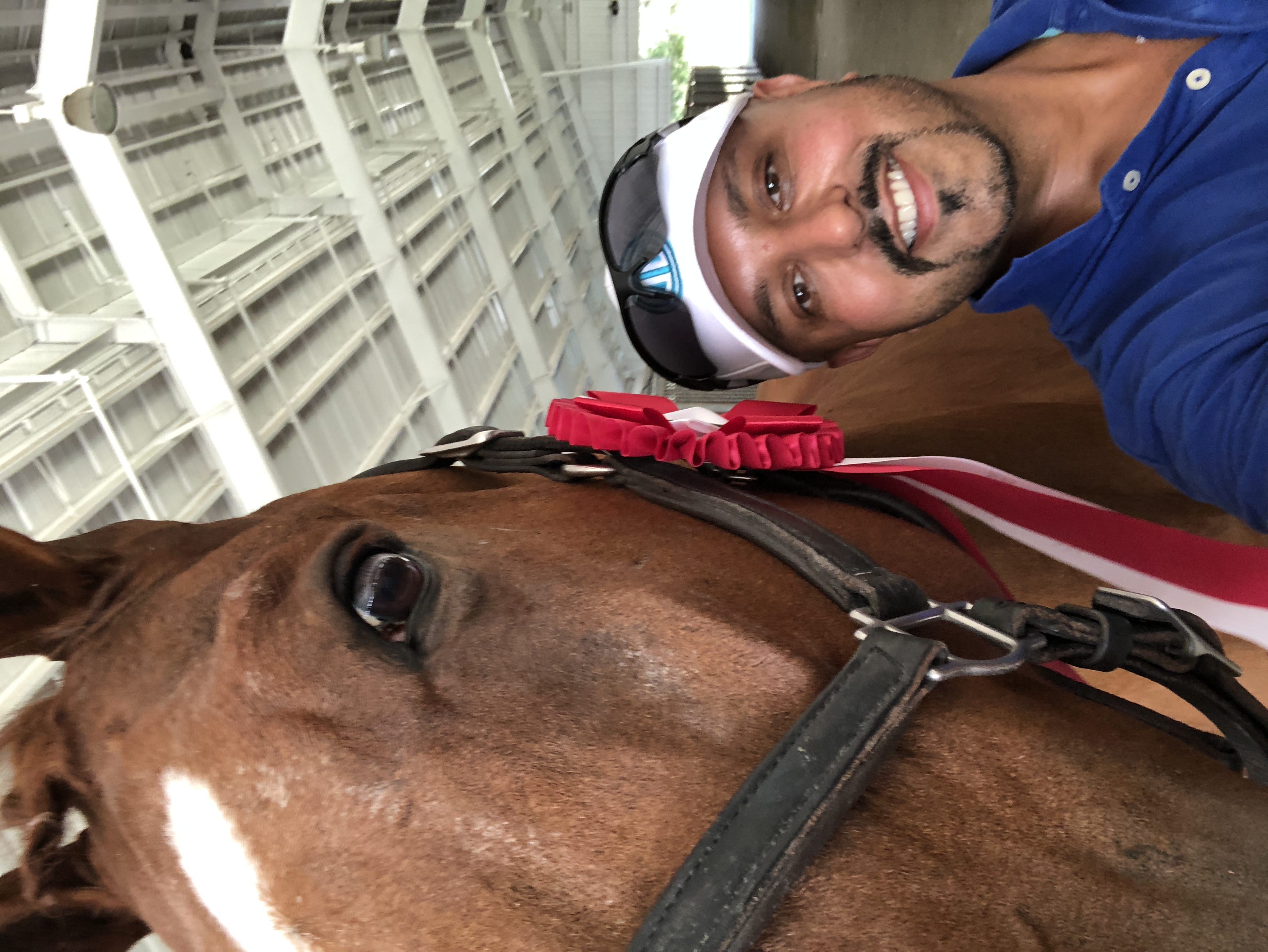 Dave Thind smiling beside a bay horse with a red award rosette