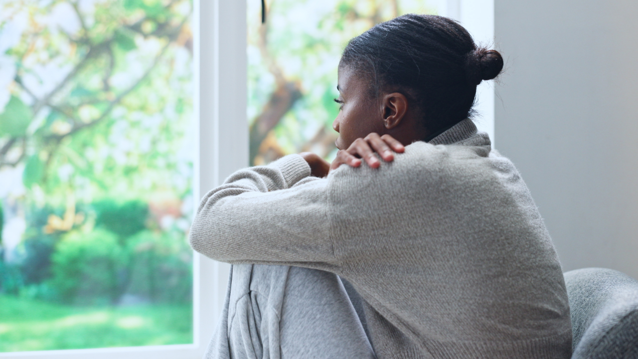 Woman sitting alone looking out a window, representing the quiet, internal struggle of postpartum psychosis