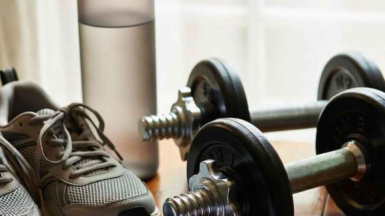 Home workout setup featuring dumbbells, athletic shoes, a water bottle, and a workout journal, illustrating strength training exercises for women over 50.
