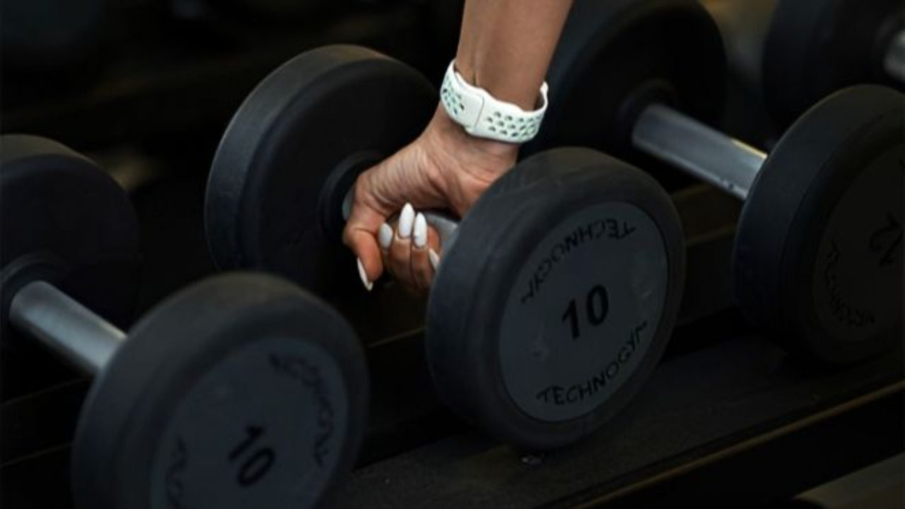 Hand reaching to lift a dumbbell from a gym rack, symbolizing strength training and focusing on body composition rather than scale weight.