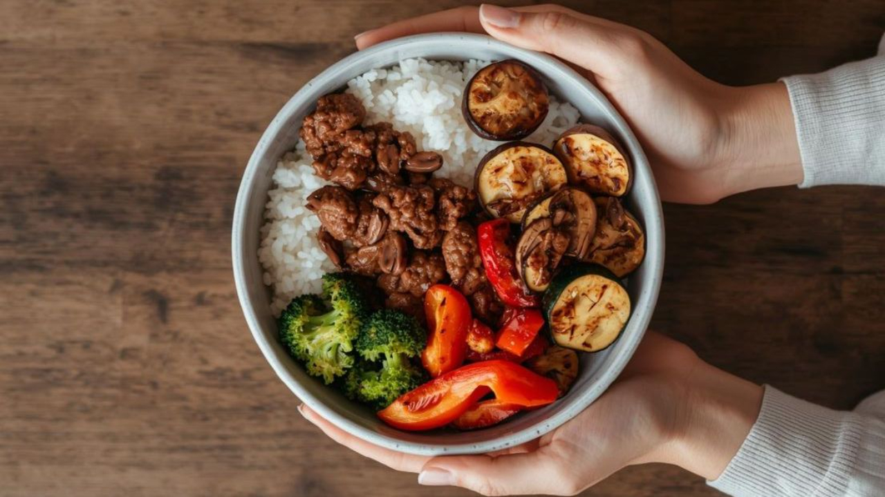A healthy protein-rich meal bowl with white rice, seasoned ground meat, broccoli, bell peppers, mushrooms, and grilled zucchini, illustrating balanced nutrition for muscle building and daily protein intake.”