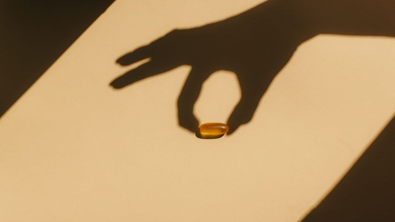 Close-up of a hand reaching toward a supplement capsule in soft natural light, representing informed choices about multivitamins and nutritional supplements for women.